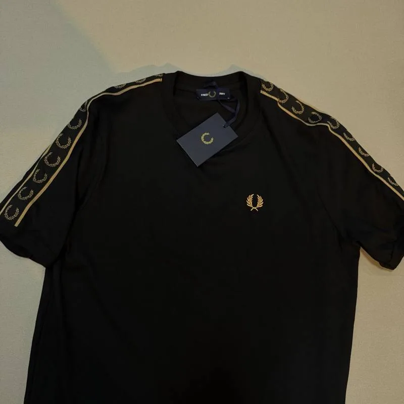 Camiseta Fred Perry preta faixa dourada nos ombros e logo dourado