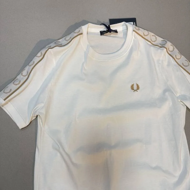 Camiseta Fred Perry branca faixa dourada nos ombros e logo dourado